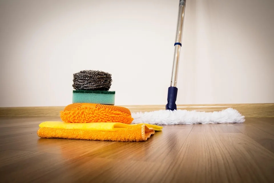 Balai de nettoyage, chiffons et éponges posés sur un parquet