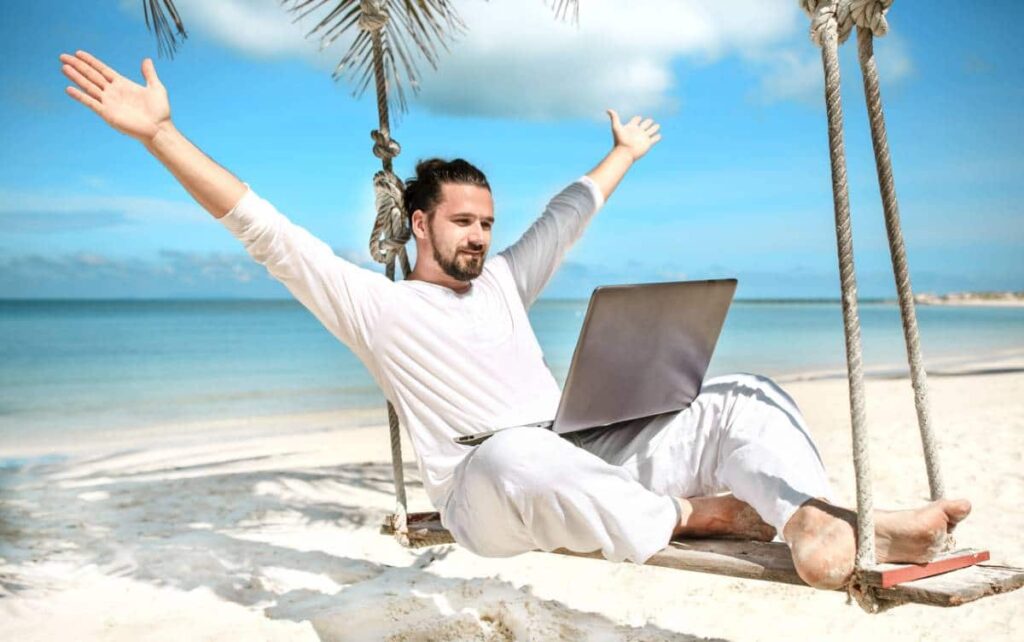 Homme les bras levés avec un ordinateur portable sur une plage