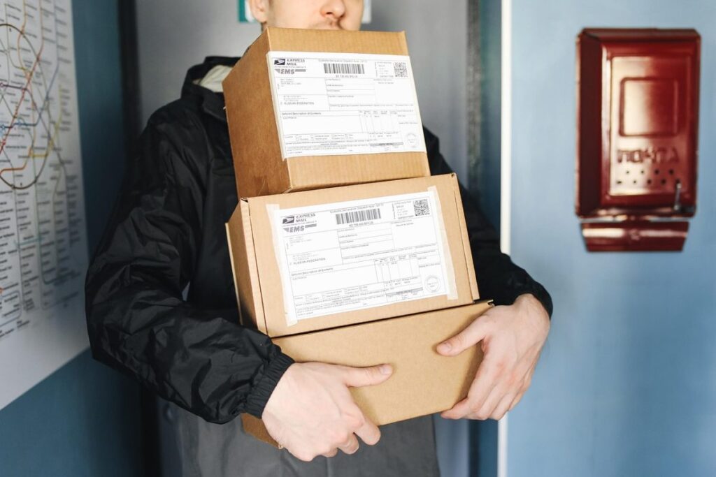 Personne portant une pile de colis en carton étiquetés
